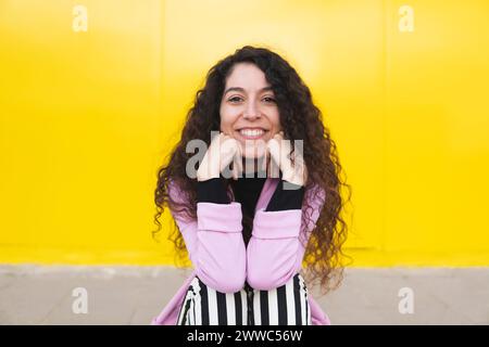 Happy woman sitting in front of yellow wall Stock Photo
