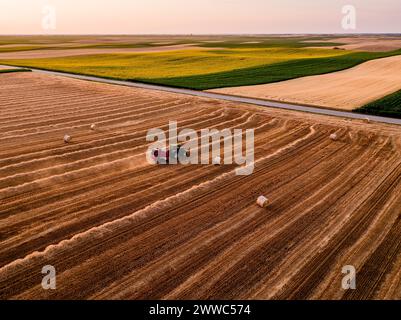 Tractor baling hay on harvested wheat field Stock Photo