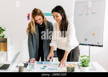 Smiling businesswoman discussing over charts and graphs with colleague in office Stock Photo