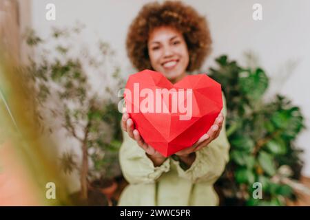 Smiling young woman holding red paper heart near plants Stock Photo