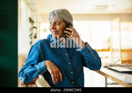 Smiling freelancer talking on smart phone at home office Stock Photo
