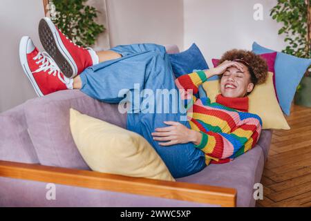 Happy young woman touching forehead and lying on sofa at home Stock Photo