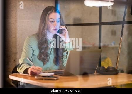 Mature businesswoman working on laptop and taking notes in office Stock Photo