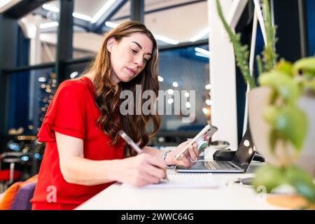Mature businesswoman writing on note pad at desk Stock Photo