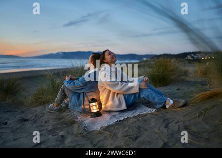 Thoughtful young couple with lantern sitting on shawl at beach Stock Photo