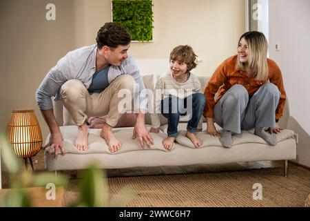 Happy mother and father crouching with son on sofa at home Stock Photo