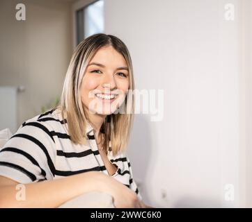 Happy young woman sitting near wall at home Stock Photo