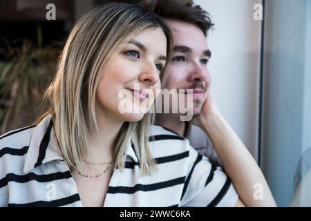 Smiling young couple looking through window at home Stock Photo