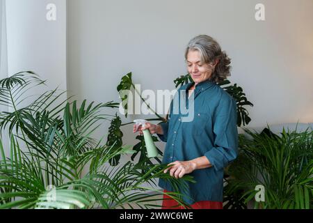 Woman spraying water with bottle on plants at home Stock Photo