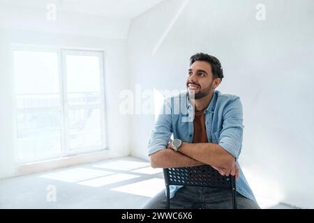 Thoughtful young man sitting on chair at new home Stock Photo
