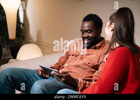 Happy man sitting with woman on sofa and using tablet PC at home Stock Photo