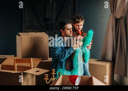 Father with son holding roll of bubble wrap near cardboard boxes Stock Photo