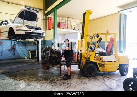 Auto mechanic dismantling engine parts near forklift at workshop Stock Photo