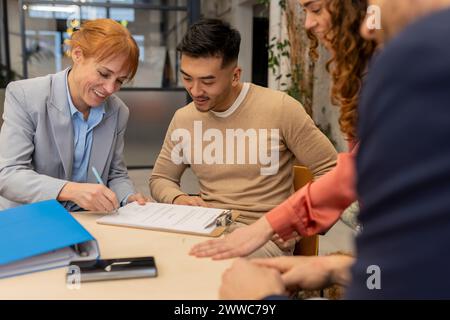 Smiling businesswoman signing contract with colleagues at co-working space Stock Photo