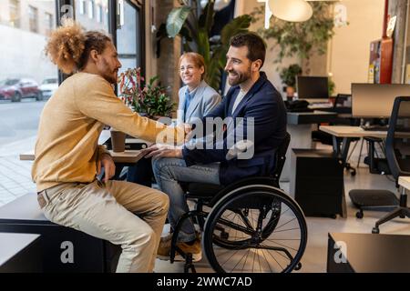 Businessman in wheelchair doing handshake with colleague at co-working space Stock Photo