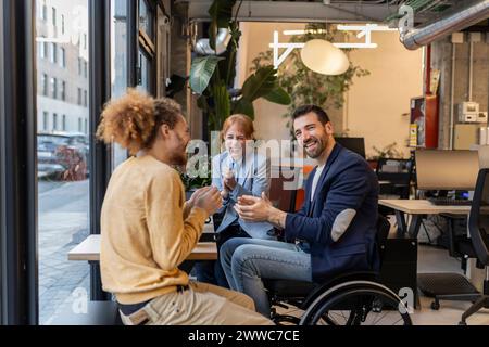 Happy manager in wheelchair applauding with colleagues at office Stock Photo