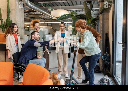 Manager in wheelchair doing handshake with colleague arriving on electric scooter at office Stock Photo