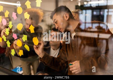 Businessman writing on adhesive note in meeting with colleagues at office Stock Photo