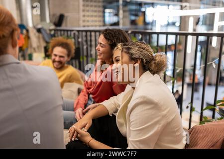 Smiling businesswoman sitting and talking with colleagues at co-working space Stock Photo