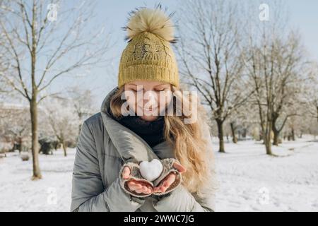 Smiling woman holding heart shaped snowball in hand Stock Photo