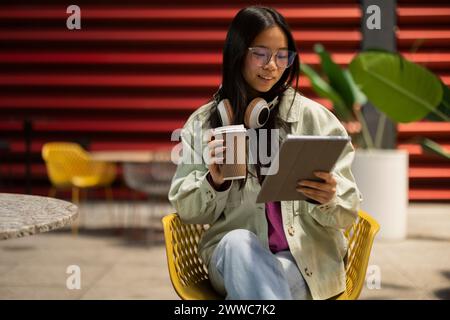 Smiling young woman holding coffee cup and using tablet PC at sidewalk cafe Stock Photo