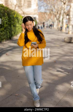 Smiling young woman wearing wireless headphones and using smart phone Stock Photo