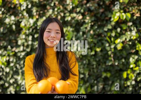 Smiling young woman holding oranges in front of plants Stock Photo