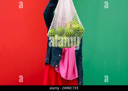 Woman holding bag of fruits in front of wall Stock Photo