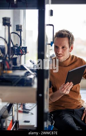 Smiling engineer holding tablet PC and looking at 3d printing machine in workshop Stock Photo