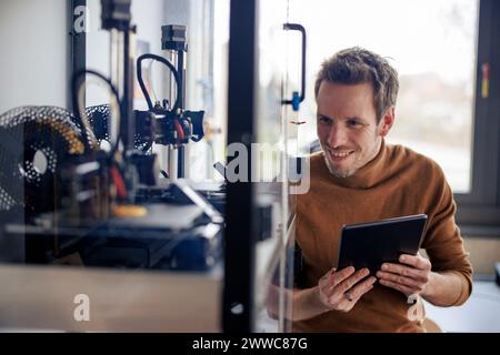 Smiling engineer holding tablet PC and looking at 3d printer in workshop Stock Photo