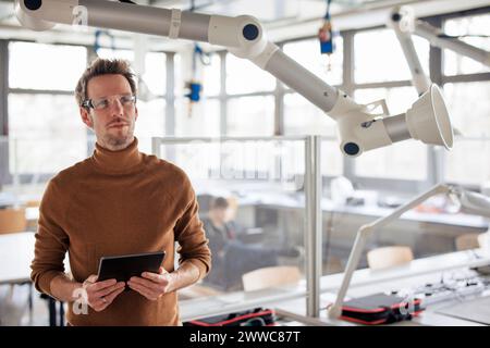 Thoughtful engineer holding tablet PC by extraction arm at workshop Stock Photo
