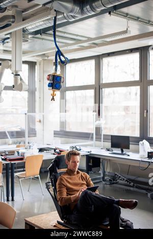 Mature engineer using tablet PC sitting on chair at workshop Stock Photo