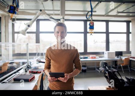 Smiling engineer holding tablet and standing at workshop Stock Photo