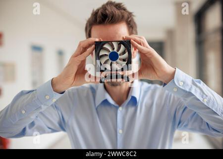Mature engineer covering face with CPU fan at workshop Stock Photo