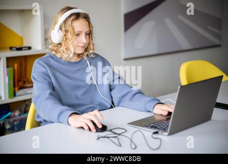 Boy wearing headphones and playing video game on laptop at home Stock Photo