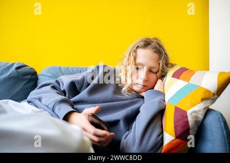 Boy lying on sofa and using smart phone at home Stock Photo