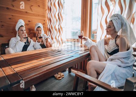 Young friends enjoying wine at table in sauna Stock Photo