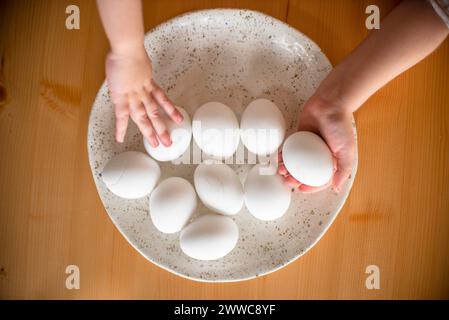 Hands of sisters holding Easter eggs in plate on table Stock Photo