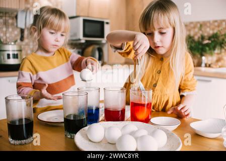 Sisters dipping Easter eggs in colored dye at home Stock Photo