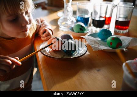 Girl decorating Easter egg with paintbrush at home Stock Photo