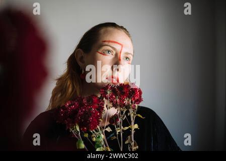 Thoughtful woman holding bunch of flowers against gray background Stock Photo