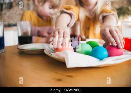 Girl arranging colorful Easter eggs in plate on table at home Stock Photo