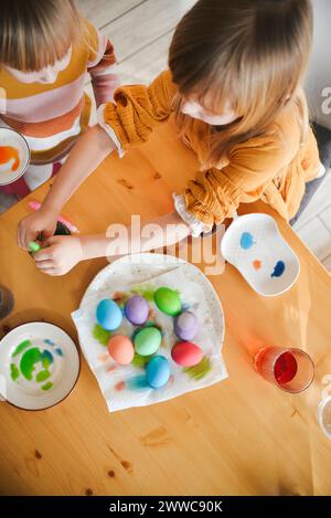 Girls coloring Easter eggs on table at home Stock Photo