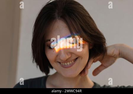 Smiling young woman with multi-colored light on face Stock Photo