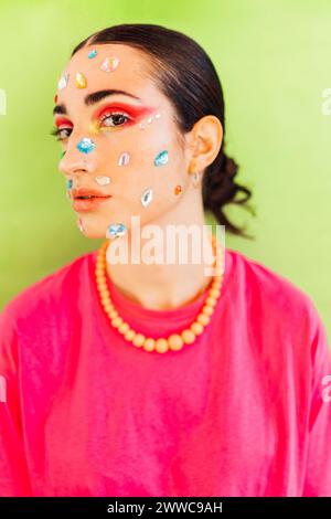 Woman with gem stickers on face against green background Stock Photo