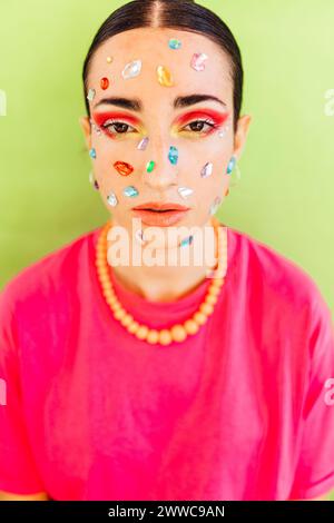 Young woman with gem stickers on face against green background Stock Photo