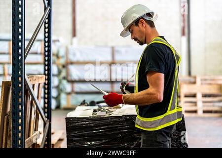 Worker wearing hardhat and examining documents at warehouse Stock Photo