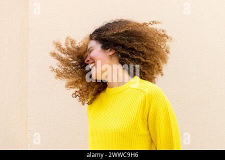 Cheerful woman tossing hair in front of wall Stock Photo