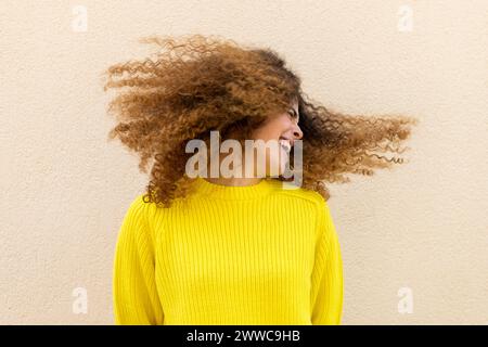 Playful woman tossing hair in front of wall Stock Photo