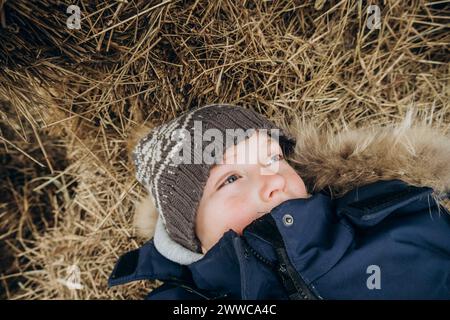 Boy wearing knit hat lying on hay at farm Stock Photo